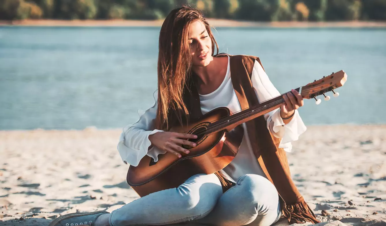 Woman exploring intuitive singing with guitar on beach
