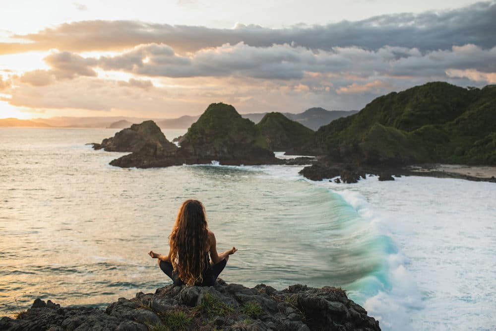 a-woman-meditating-on-the-beach-near-mountains