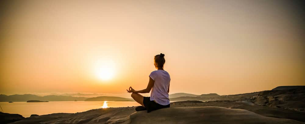 a-woman-meditating-on-the-beach-watching-the-sunset