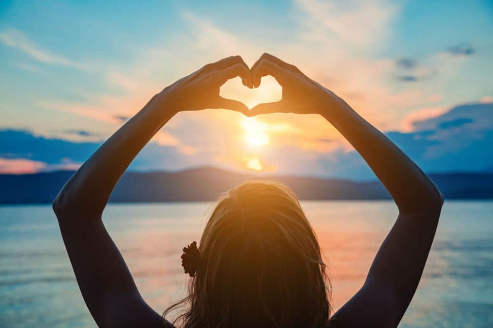 a-woman-holding-up-a-heart-during-the-sunrise