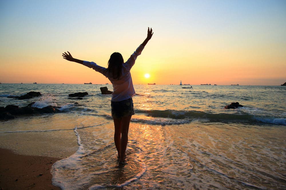 a-woman-smiling-on-the-beach-watching-the-sunset