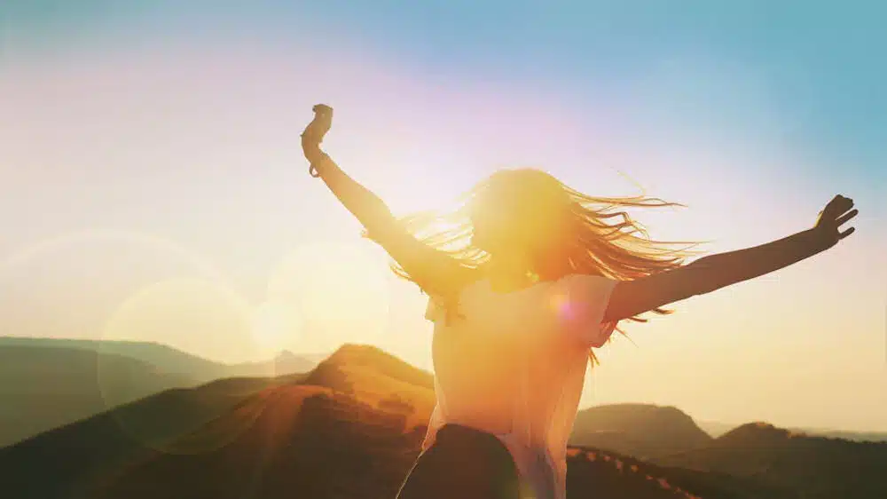 joyful woman raising her hands with sunset at background
