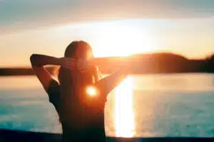 a-woman-with-her-hands-behind-her-head-on-the-beach-watching-the-sunrise