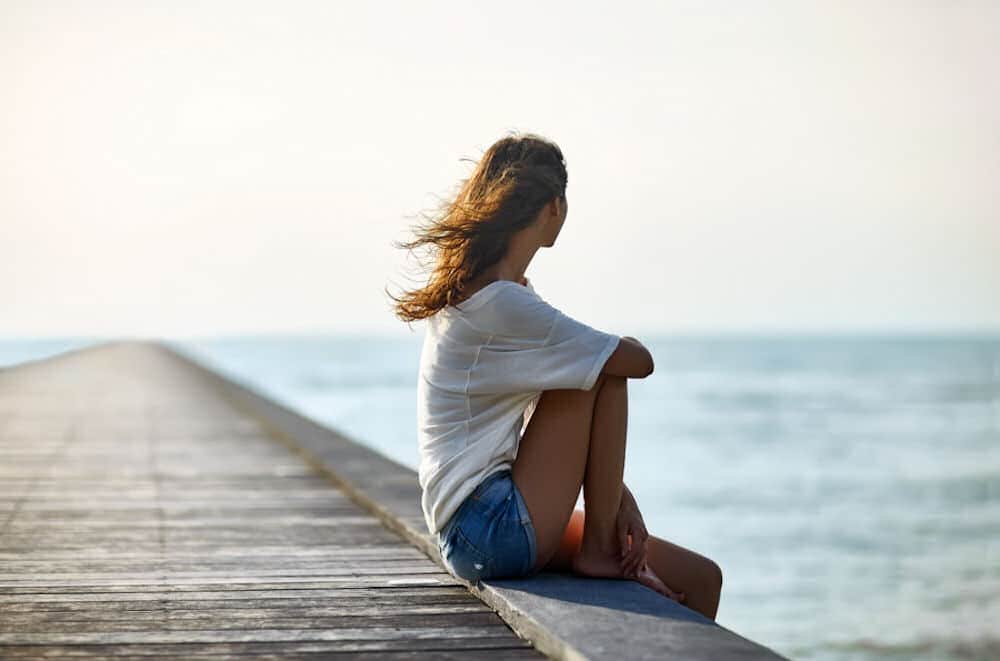 a-woman-sitting-on-a-pier-staring-off