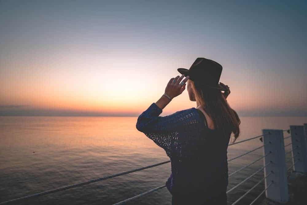 a-woman-with-a-hat-on-holding-it-at-the-beach