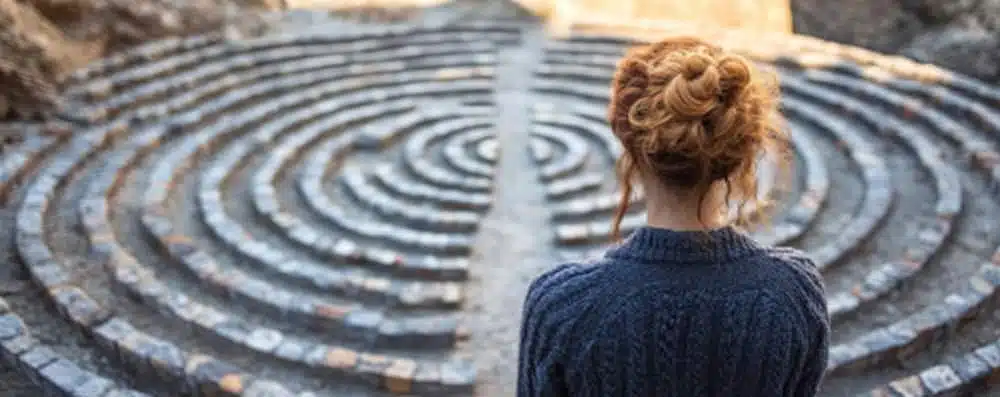 A woman stands thoughtfully in front of a complex labyrinth, contemplating her next move in the intricate maze.