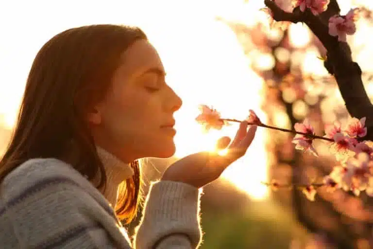 a woman with her eyes closed smelling a flower